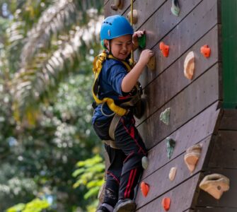 a boy with blue helmet climbing on a wooden wall