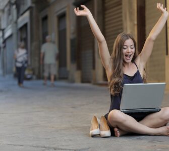 woman raising her hands up while sitting on floor with macbook pro on lap