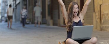 woman raising her hands up while sitting on floor with macbook pro on lap