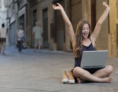 woman raising her hands up while sitting on floor with macbook pro on lap