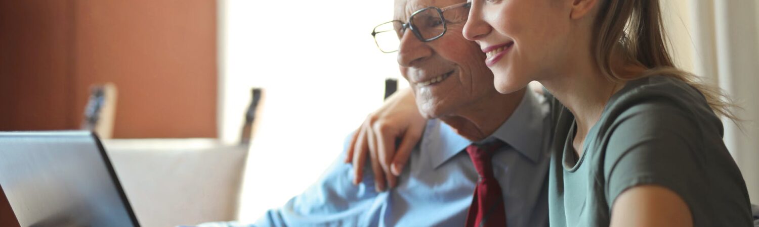 young positive woman helping senior man using laptop