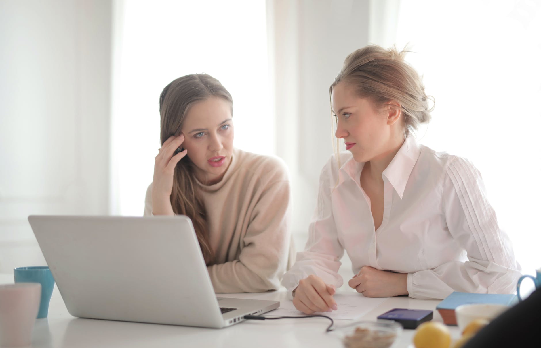 thoughtful businesswomen discussing problems in bright workspace