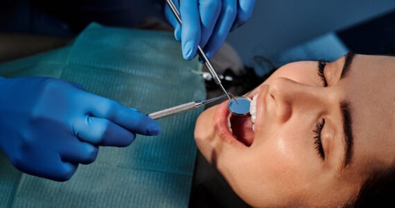 a person wearing blue latex gloves holding a mirror in a woman s mouth