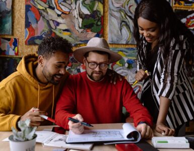 men and woman discussing project in a sketchbook and abstract paintings hanging on a wall