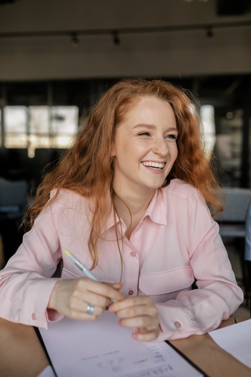 close up photo of a woman with red hair laughing while holding a pen